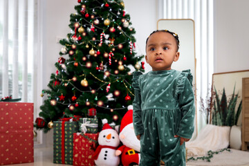 Portrait of adorable African American little girl child standing in living room with many gift boxes presents under Christmas tree, kid celebrating happy Christmas winter holiday