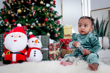 Portrait of adorable African American little girl child sitting on white carpet at living room floor with many gift boxes presents under Christmas tree, kid celebrating happy Christmas winter holiday.