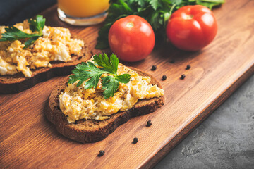Scrambled eggs with parsley on bread, homemade healthy breakfast on dark wooden board