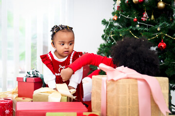 Fototapeta na wymiar Two adorable happy smiling African American little girl sisters with black curry hair hold many gift boxes presents under Christmas tree in living room, kid celebrating happy Christmas winter holiday