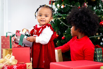 Two adorable happy smiling African American little girl sisters with black curry hair hold many gift boxes presents under Christmas tree in living room, kid celebrating happy Christmas winter holiday