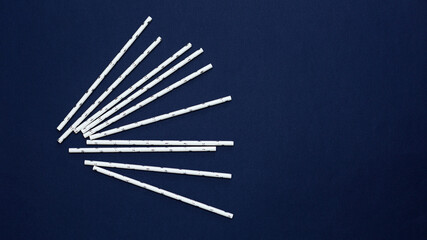 Paper straws are  white with silver stars for drinks on dark blue background. Concept: christmas, new year, birthday, parties. Copy space. Top view