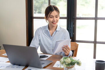 Female freelance is reading information of business on notebook and typing data on laptop while working