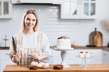 Pastry chef confectioner young caucasian woman with knife cut slice cake on kitchen table. Cakes cupcakes and sweet dessert