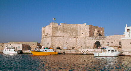 Fototapeta premium Castillo de Carlos V en el puerto de Monopoli, Italia. Viejo puerto con sus barcos anclados o atracados en el muelle y rodeado de los edificios antiguos de arquitectura medieval.