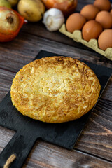 Top view, still life. Spanish potato omelette with some ingredients, on a wooden background.