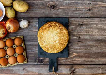 Top view, still life. Spanish potato omelette with some ingredients, on a wooden background. Space for text.