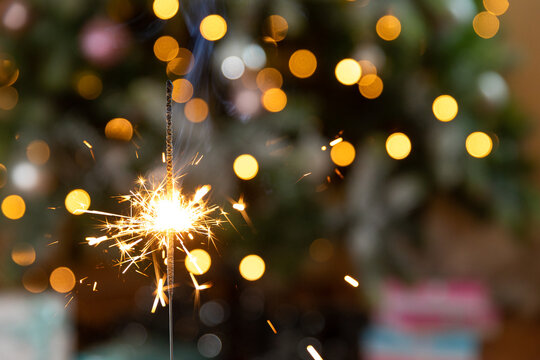 Christmas Glittering Sparklers Candle Burns In Christmas Tree Background. Xmas Lighting Decoration At Home Indoor. Festive Magic Sparks Lights For Holiday Party. Christmas Eve With Fireworks