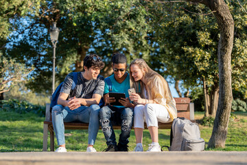 Group of teenage friends looking at a tablet in the park sitting on a bench