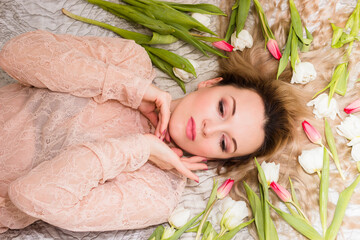 Naklejka premium Portrait of a young woman on a bed with tulips in her hair