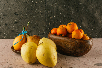 Winter season fruit in Mexico, Tejocotes on a wooden bowl, mucus grenades on a wooden plate and giant guavas on a pink quarry background.