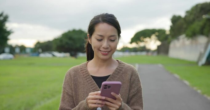 Woman hold with mobile phone and walk in the park
