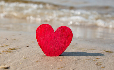 Fototapeta premium Tropical background for Valentine's Day. The red wooden heart is located on the sandy beach. Behind the sea or ocean. Love for travel