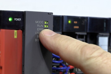 PLC - Programmable logic controller. LED indicators. The hand shows the operation of the system. Program run. Production automation. Testing and programming of an industrial control system.