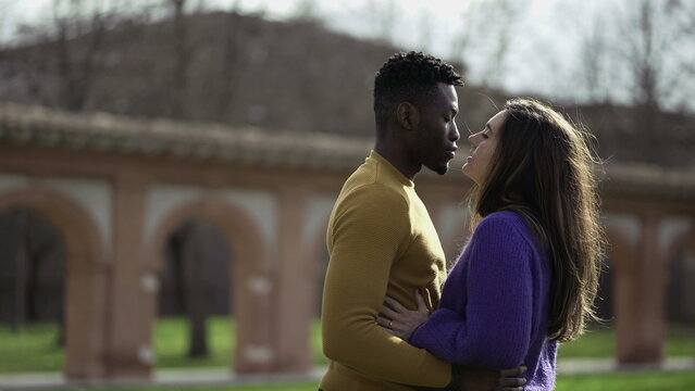 Black man kissing white girlfriend standing outside at park