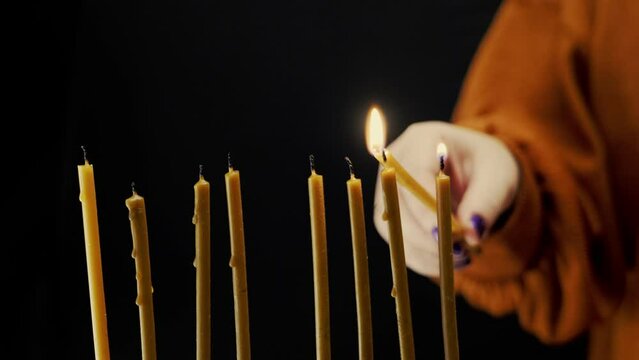 A woman's hand lights candles on the last day of Hanukkah from a shamash candle in a Hanukkah candlestick. Medium plan