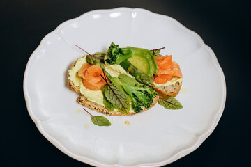 Toast with salmon and broccoli, garnished with herbs and sauce.