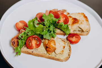 Bruschetta with prosciutto sauce and chicken fillet, garnished with greens and tomatoes.