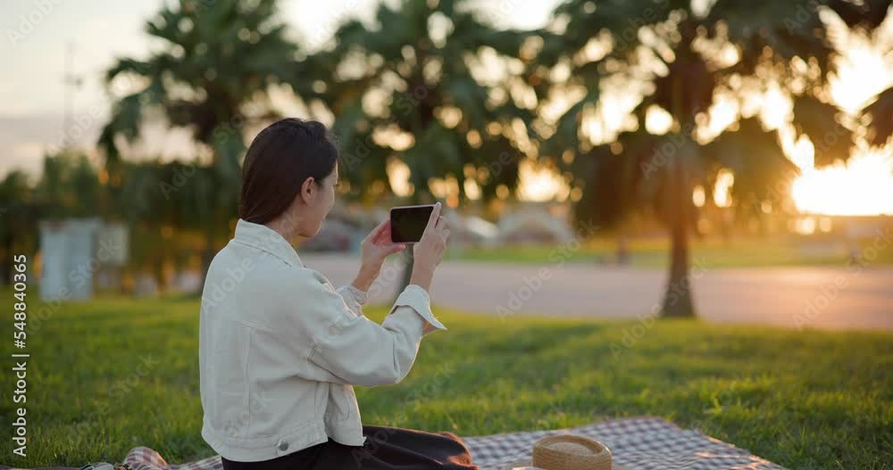 Wall mural woman go picnic and use cellphone to take photo at sunset time