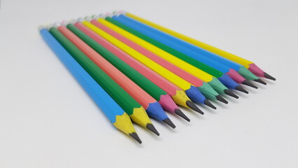 A selection of blue, yellow, pink and green hexagon shaped pencils with coloured erasers lined up...