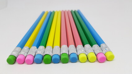 A selection of blue, yellow, pink and green hexagon shaped pencils with coloured erasers lined up...