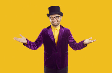 Friendly entertainer in purple costume welcomes you to circus show or theatrical performance. Happy man in suit, hat and glasses standing isolated on yellow background, spreading arms and smiling