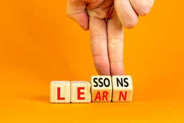 Lessons to learn symbol. Concept word Lessons learn on wooden cubes. Beautiful orange table orange background. Businessman hand. Business education and lessons to learn concept. Copy space.