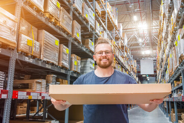 Caucasian young male smiling in glasses is warehouse worker holding and giving box to customer,...
