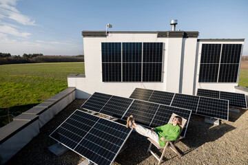 Young woman sits relaxed on a lounge chair while resting on rooftop with a solar station. Happy...