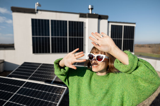 Woman plays with a sun, shading her face with hands, while standing on rooftop with a solar power plant. Concept of a happy household owner and sustainable lifestyle