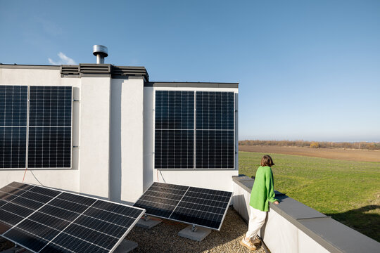 Woman on the rooftop of her house with a solar power plant installed on it. Happy owner of energy-independent household