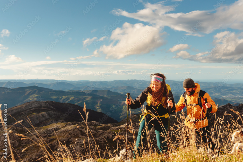 Wall mural couple of hikers equipped with backpacks, trekking poles and warm clothes doing a mountain route. ou