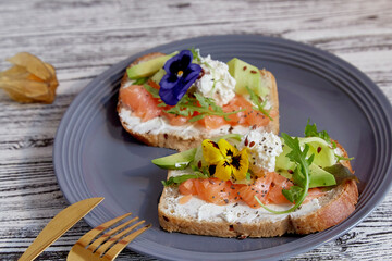 Couple of sandwiches with salmon, avocado and edible flowers. Healthy breakfast.Pescetarian diet.