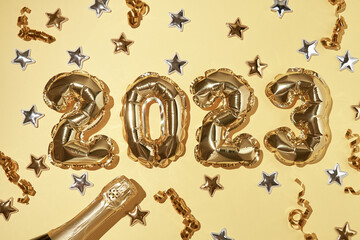 Foil gold air balloons in the form of number 2023 on yellow background with confetti stars and party streamers. New year and christmas celebration. Top view, horizontal, copyspace.