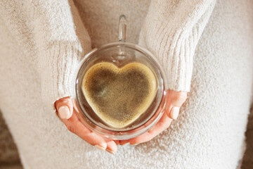 Cup of coffee with foam in female hands. Heart shape. Top view.