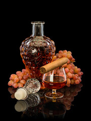 Open decanter and glass filled with cognac, cigar and bunch of grapes