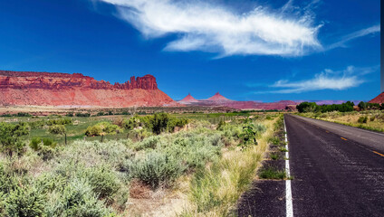 Empty road to Monument Valley, Utah, Arizona, red mesa mountain, dry green grass, blue summer sky