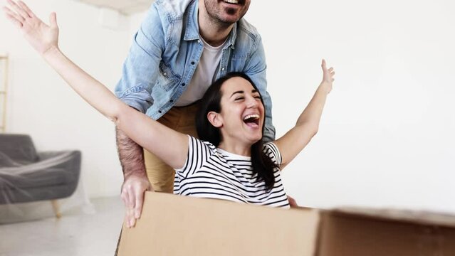 Happy couple having fun while unpacking on moving day in new apartment - First day at new house of funny man and woman - Moving and relocation concept. High quality 4k footage