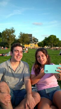 young caucasian woman and man student friends relaxing, having fun in the park and taking photos