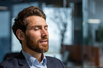 Obraz premium Mature businessman boss with eyes closed meditating and breathing in office, man with beard and business suit dreaming and visualizing inspiration.