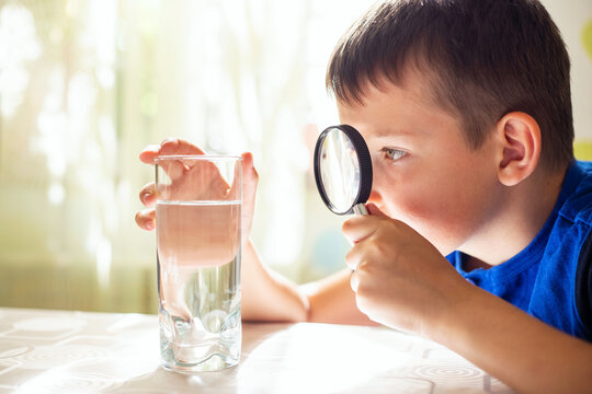 The Child Boy Looking At Water In A Glass Through Magnifying Glass