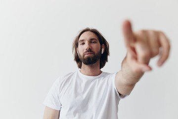 happy man listening to music and smiling in a white t-shirt on a white background and pointing a finger at the screen at the camera