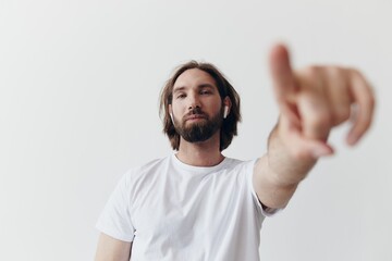 happy man listening to music and smiling in a white t-shirt on a white background and pointing a...