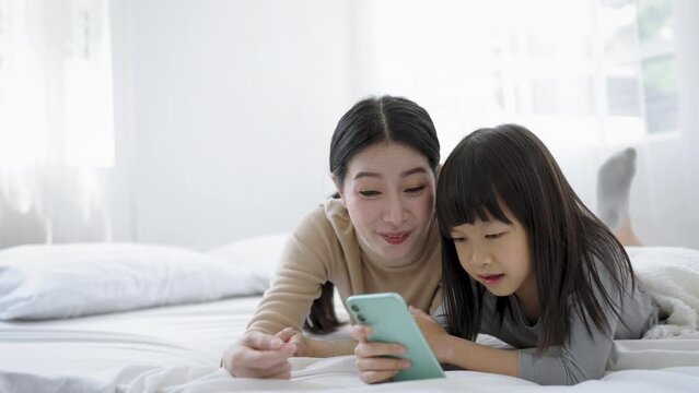 Young happy woman with cute little daughter taking photo selfie with mobile phone, enjoying technology network together at home bedroom, happy family mothers day, education technology concept