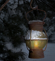 Old snow covered lantern hanging near a tree