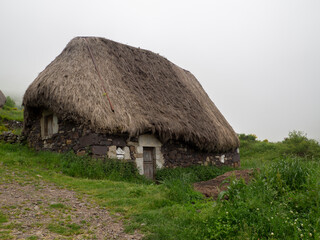 Fototapeta na wymiar Vistas de una casa tiípica en la Braña de Pornacal, de Asturias, con techo de paja en verano, un día de niebla blanca y césped verde, España, 2021