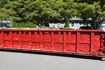 Fototapeta na wymiar Side view of a large red beat up dumpster on the street by a curb in a residential development
