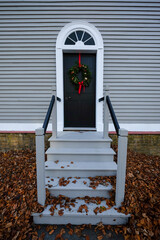 The exterior wall of a tan wooden clapboard house with a black wooden door with a colorful silk...