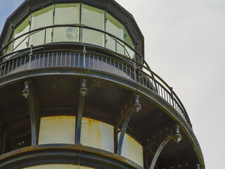 Fototapeta premium Close-up. A huge tower of a high lighthouse against a cloudy sky. Beautiful building, interesting architecture. Construction, infrastructure, tourism, travel.