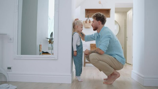 Cute blond father measuring her daughter's height at home